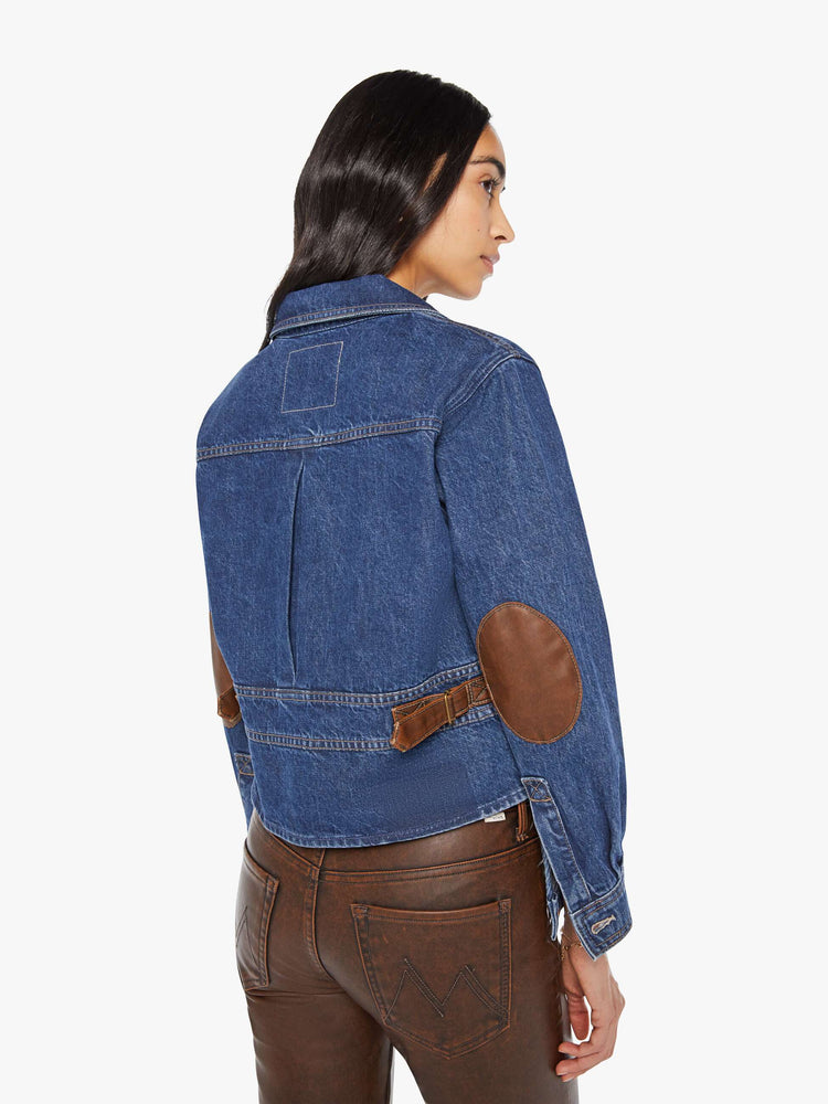 Back view of a woman in a denim jacket with brown faux-leather patches on the shoulders and adjustable tabs on the waist.