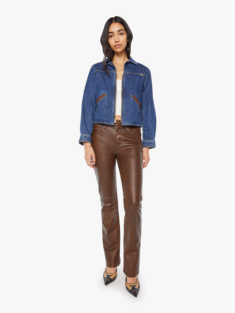 Full body view of a woman in a denim jacket with brown faux-leather patches on the shoulders and adjustable tabs on the waist.