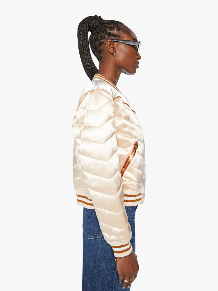 Side view of a woman letterman jacket has ribbed hems, slit pockets and a slightly cropped fit in a baby pink with white and orange detailing.