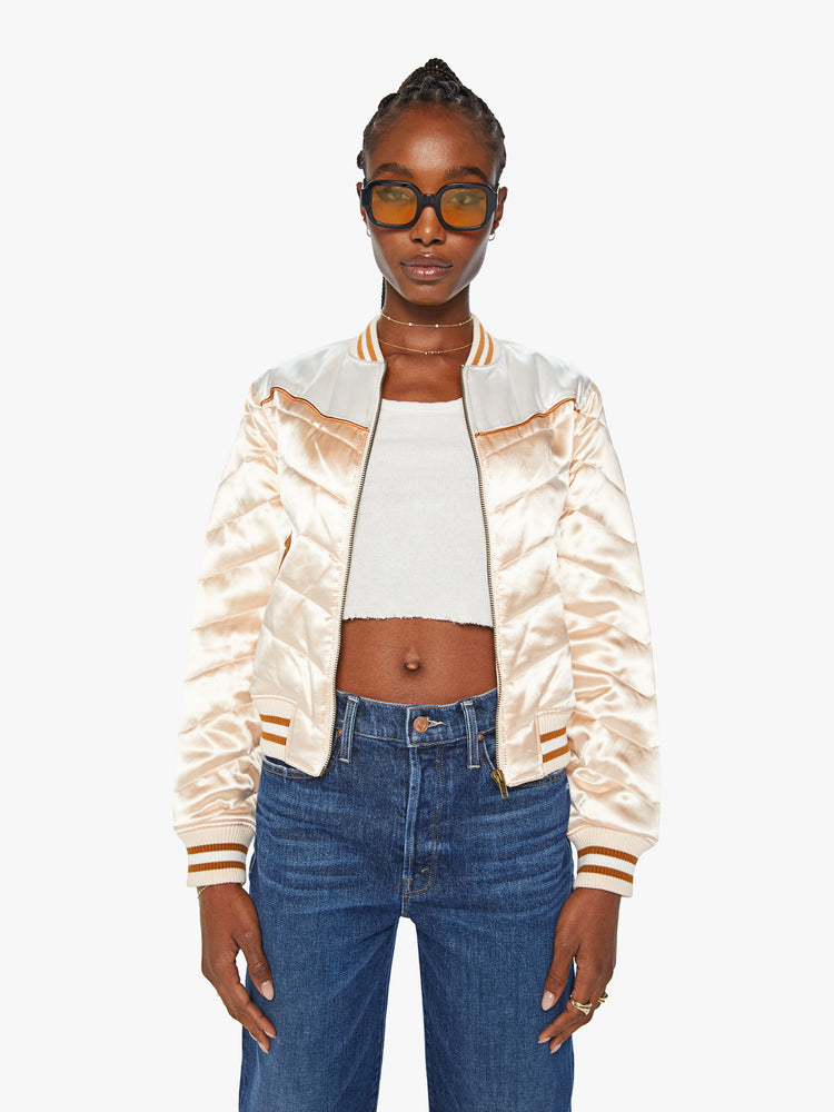 Front view of a woman letterman jacket has ribbed hems, slit pockets and a slightly cropped fit in a baby pink with white and orange detailing.