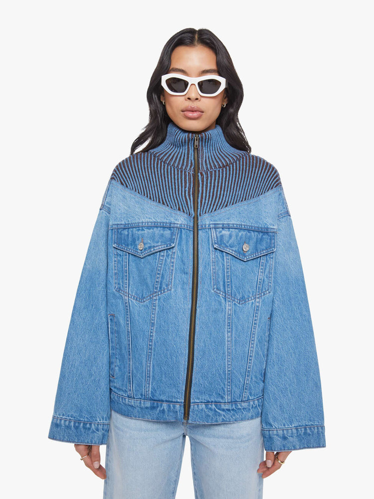 Front view of a woman in a half denim jacket, half sweater with ribbed details around the neck, chest and shoulders, a high collar, drop shoulders, extra-wide long sleeves, front patch pockets and a super boxy fit. 
