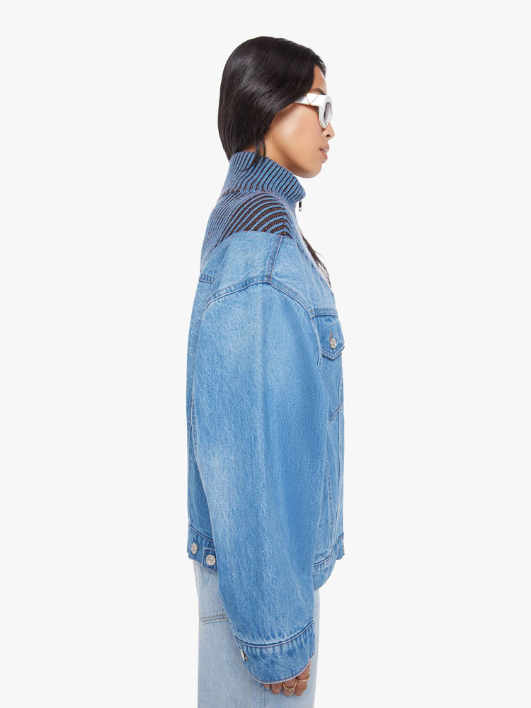 Side view of a woman in a half denim jacket, half sweater with ribbed details around the neck, chest and shoulders, a high collar, drop shoulders, extra-wide long sleeves, front patch pockets and a super boxy fit. 