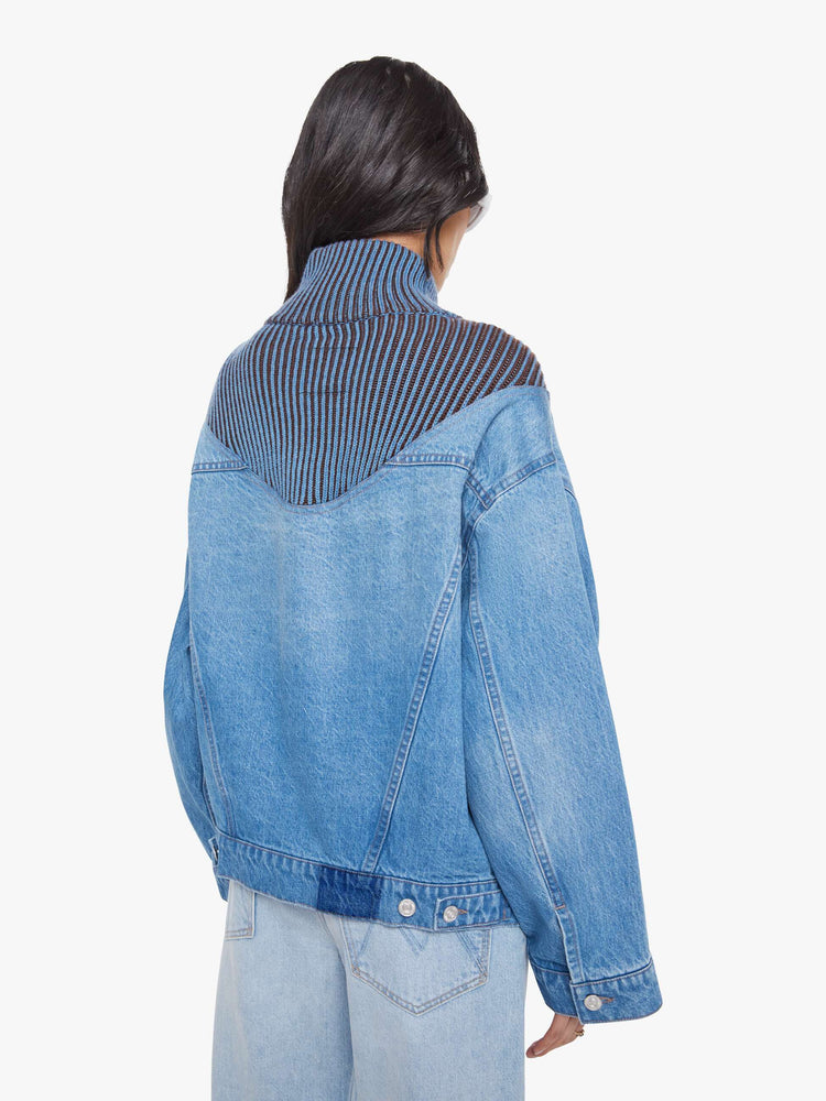 Back view of a woman in a half denim jacket, half sweater with ribbed details around the neck, chest and shoulders, a high collar, drop shoulders, extra-wide long sleeves, front patch pockets and a super boxy fit.