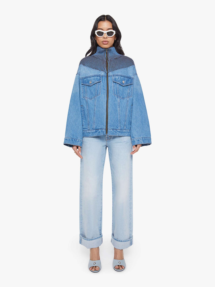 Full body view of a woman in a half denim jacket, half sweater with ribbed details around the neck, chest and shoulders, a high collar, drop shoulders, extra-wide long sleeves, front patch pockets and a super boxy fit. 