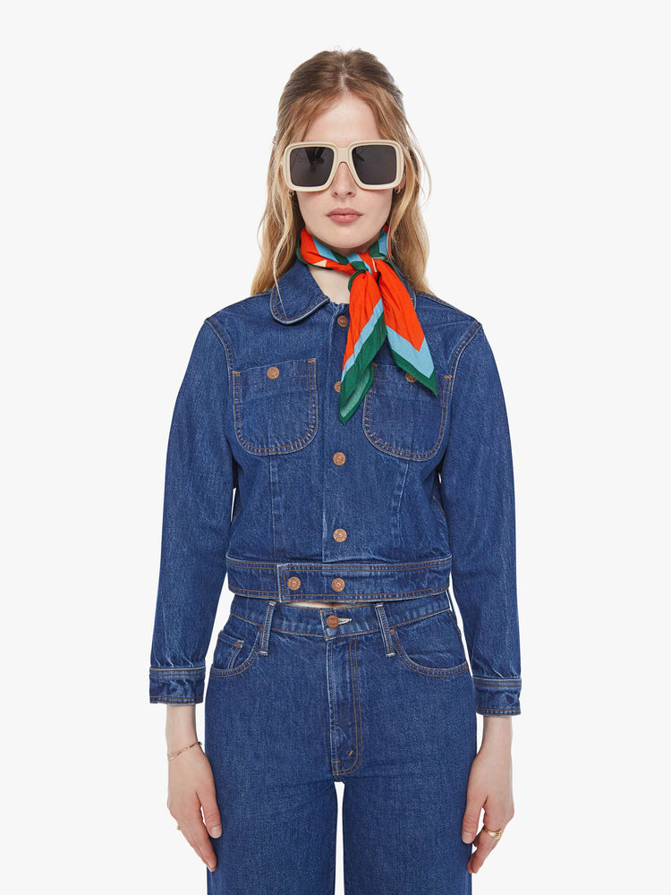 Front view of a woman in a mid blue shrunken denim jacket with patch pockets and a cropped hem. 