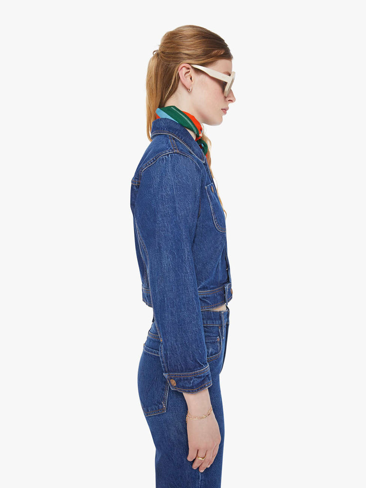 Side view of a woman in a mid blue shrunken denim jacket with patch pockets and a cropped hem. 