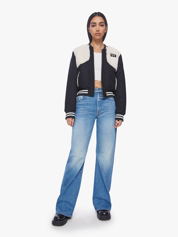 Front full body view of a woman dark blue with white faux-sherpa details on the shoulders and striped hem zip-up varsity bomber jacket.