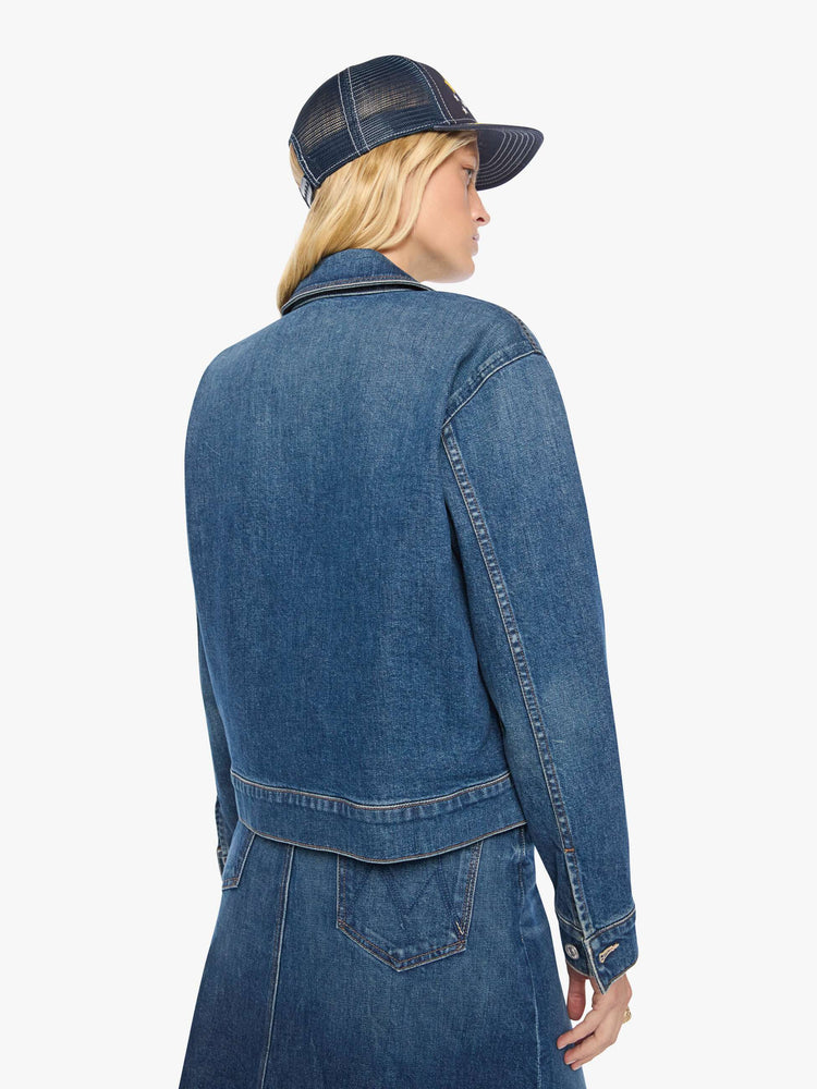 Back view of a woman in a med blue denim jacket with a Western-inspired yoke, sawtooth pointed patch pockets on the chest and a cropped, boxy fit.