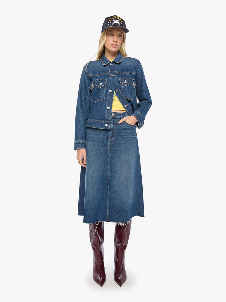 Full body view of a woman in a med blue denim jacket with a Western-inspired yoke, sawtooth pointed patch pockets on the chest and a cropped, boxy fit.