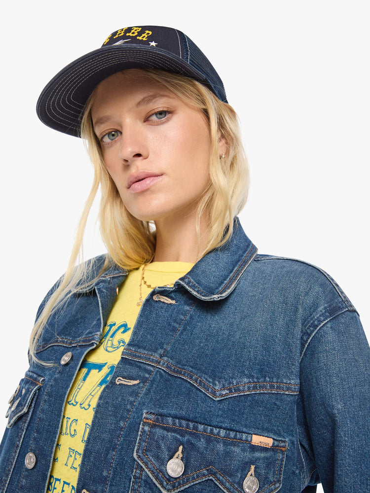 Clos up view of a woman in a med blue denim jacket with a Western-inspired yoke, sawtooth pointed patch pockets on the chest and a cropped, boxy fit.