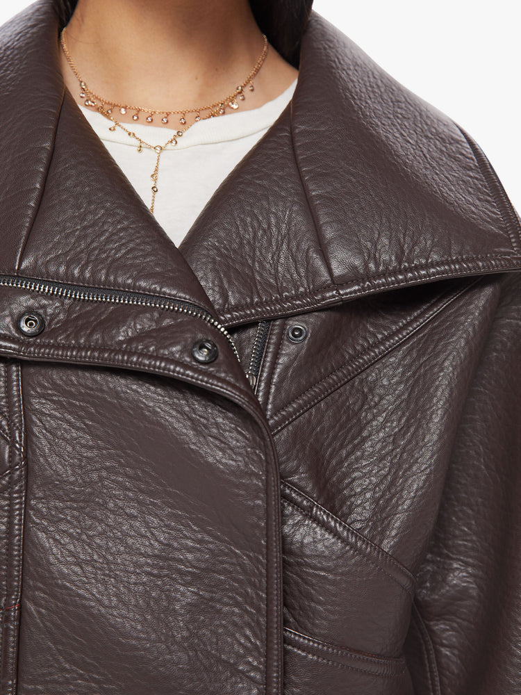 Close up view of a woman brown faux leather jacket with a dramatically oversized collar, front slit pockets, drop shoulders and a hidden zip closure with buttons down the front.