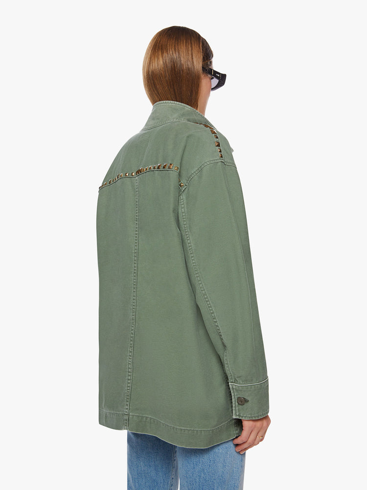 Back view of a woman army-green hue with studded details on the front and yoke of an oversized military jacket with patch pockets, drop shoulders and buttons down the front.