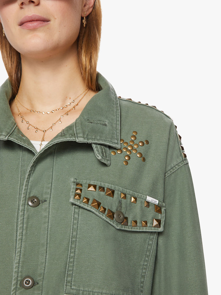 Front close up view of a woman army-green hue with studded details on the front and yoke of an oversized military jacket with patch pockets, drop shoulders and buttons down the front.