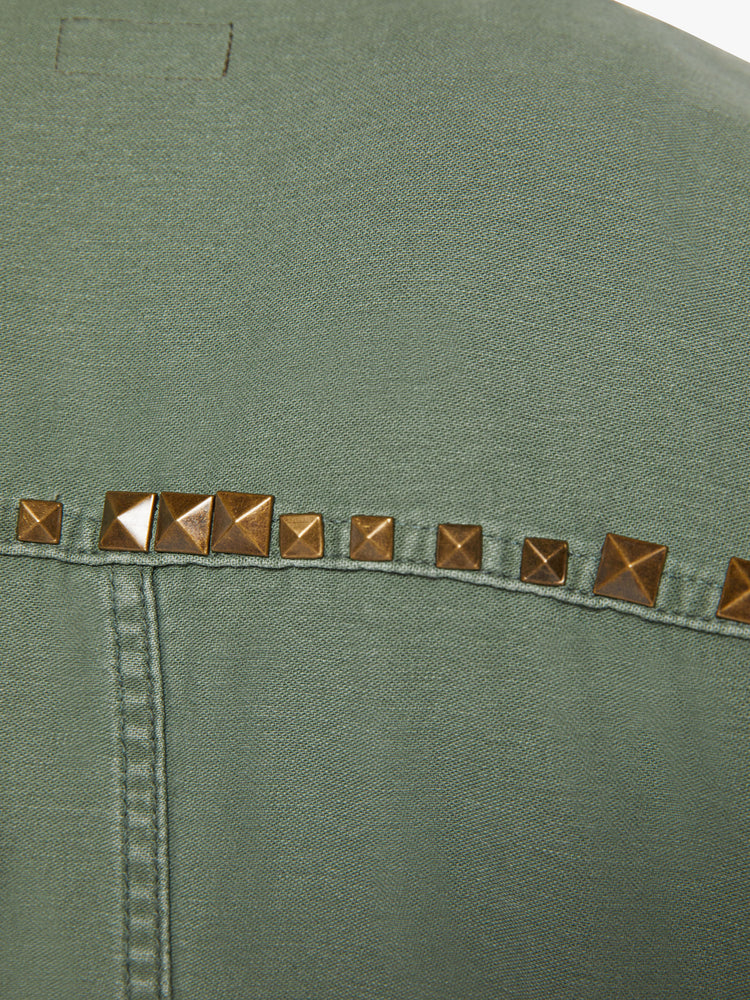 Studded close up view of a woman army-green hue with studded details on the front and yoke of an oversized military jacket with patch pockets, drop shoulders and buttons down the front.