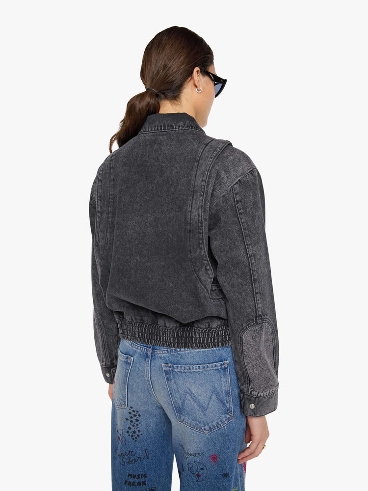 Back view of a woman in a faded grey  jacket is designed with drop shoulders, seamed details, hidden Velcro pockets, an elastic hem and a zip closure with a button flap. 