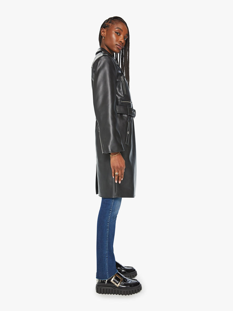 Side view of woman black motorcycle trench coat with a notched collar, belted waist, zip closure and a thigh-grazing hem.