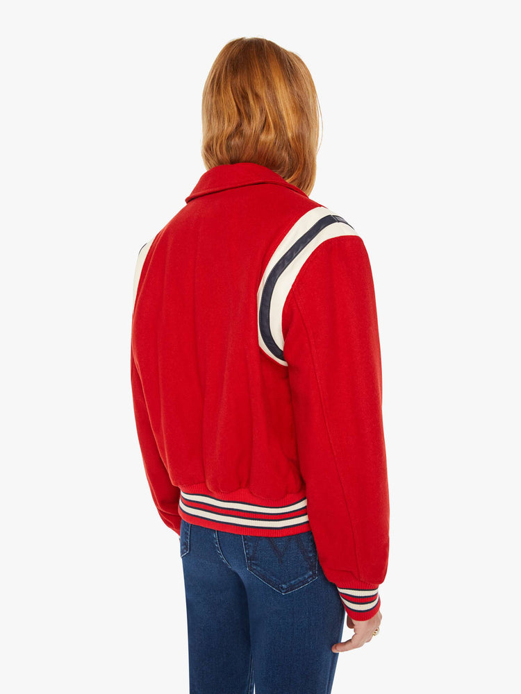 Back view of a woman red vintage-inspired varsity jacket with drop shoulders, slit pockets, ribbed hems and snaps down the front with faux leather stripes on the shoulders and a M shaped patch.