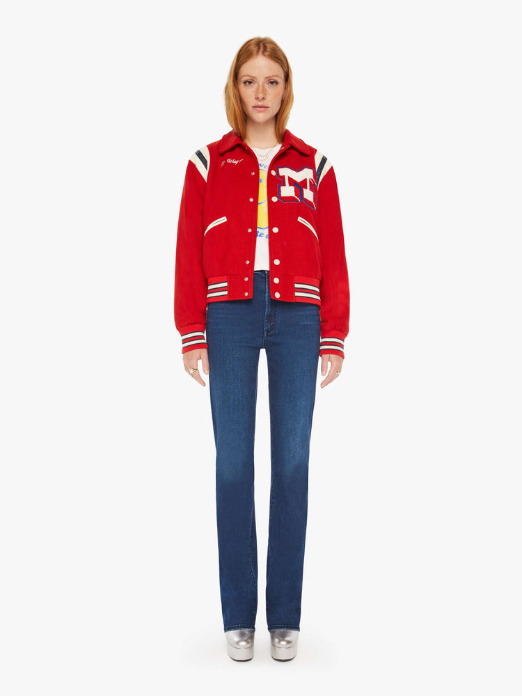 Full body view of a woman red vintage-inspired varsity jacket with drop shoulders, slit pockets, ribbed hems and snaps down the front with faux leather stripes on the shoulders and a M shaped patch.