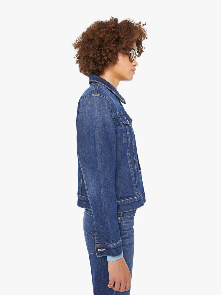 Side view of a woman in a dark blue  denim jacket with front patch pockets and a slightly cropped fit. 