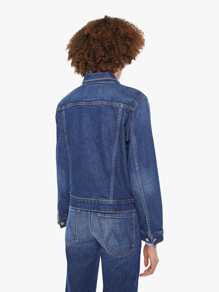Back view of a woman in a dark blue  denim jacket with front patch pockets and a slightly cropped fit. 