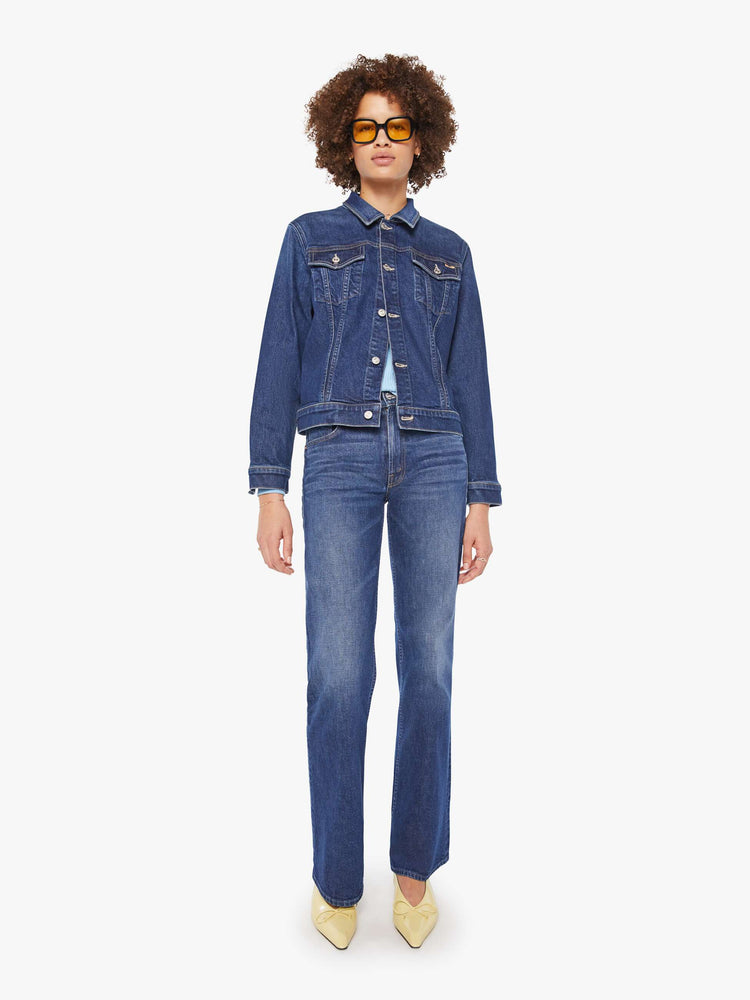 Full body view of a woman in a dark blue  denim jacket with front patch pockets and a slightly cropped fit. 