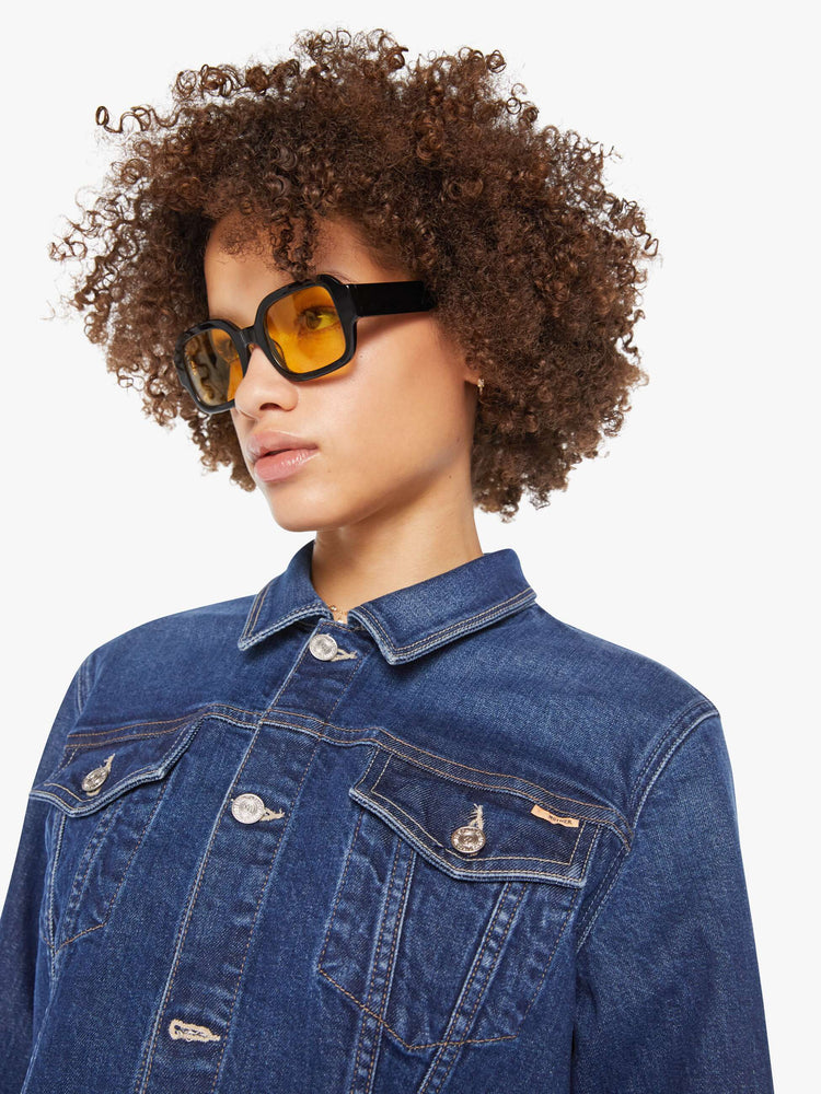 Close up view of a woman in a dark blue  denim jacket with front patch pockets and a slightly cropped fit. 