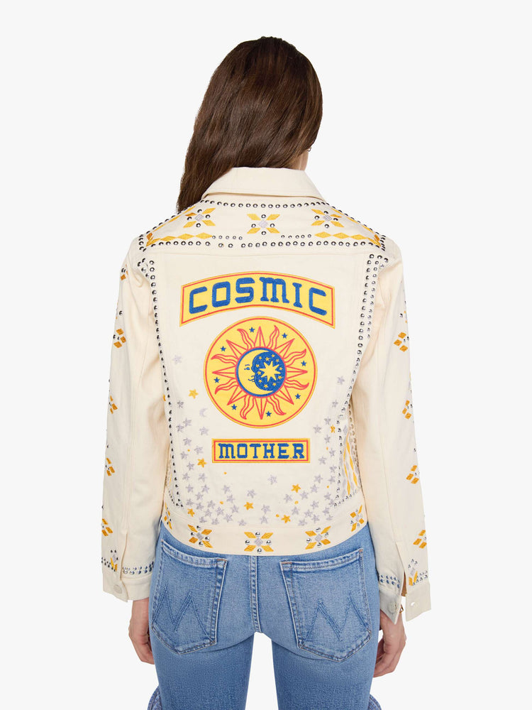 Back view of a woman in a warm cream with silver and golden-yellow embroidery, decorative rivets and oversized patches on the back, classic button-up jacket with front patch pockets and a slightly cropped fit.