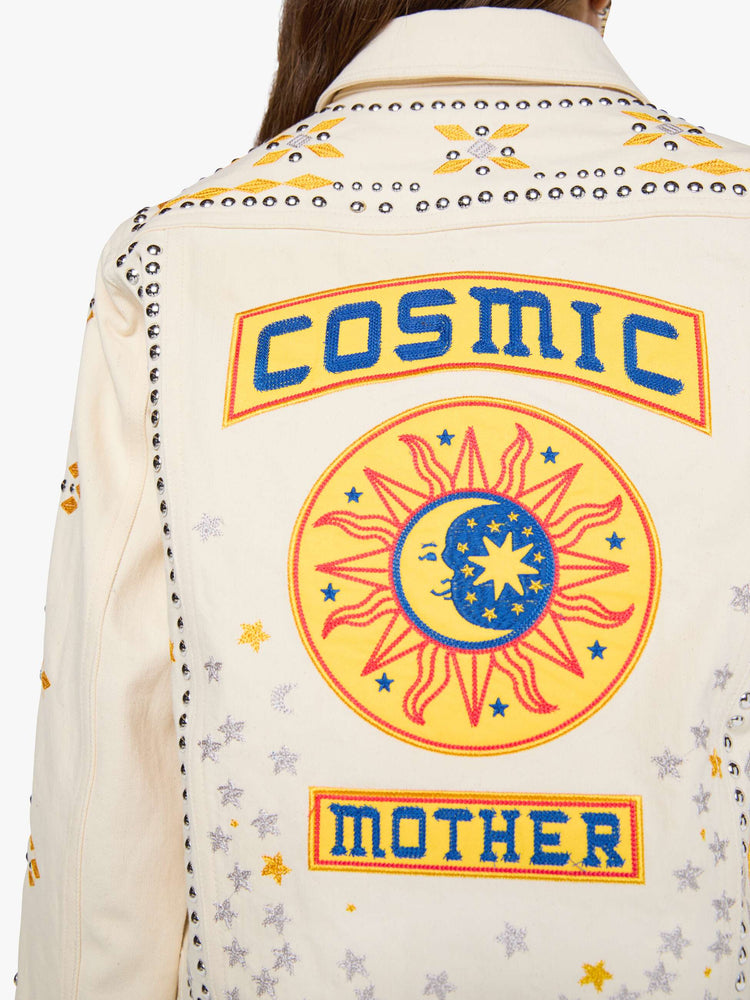 Close up view of a woman in a warm cream with silver and golden-yellow embroidery, decorative rivets and oversized patches on the back, classic button-up jacket with front patch pockets and a slightly cropped fit.