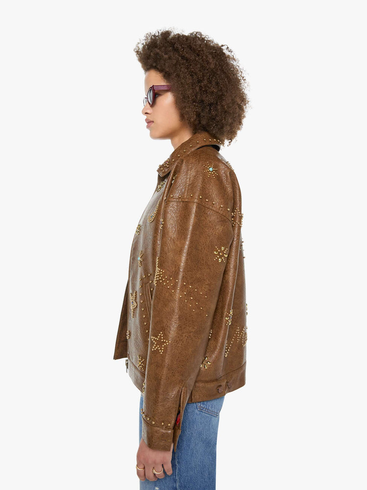 Left side view of a woman in a brown faux leather with celestial rhinestone details boxy jacket with drop shoulders, a zip closure and an oversized fit.
