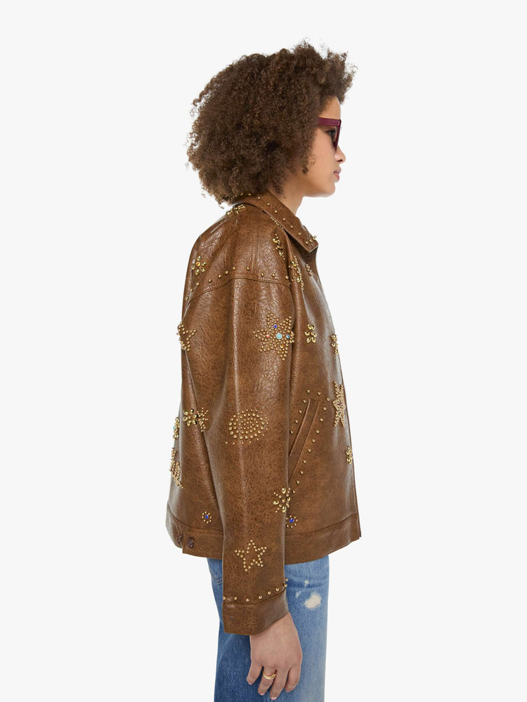 Side view of a woman in a brown faux leather with celestial rhinestone details boxy jacket with drop shoulders, a zip closure and an oversized fit.