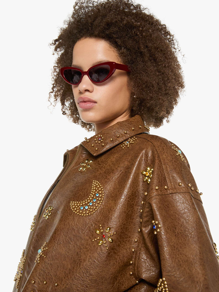 Close up view of a woman in a brown faux leather with celestial rhinestone details boxy jacket with drop shoulders, a zip closure and an oversized fit.
