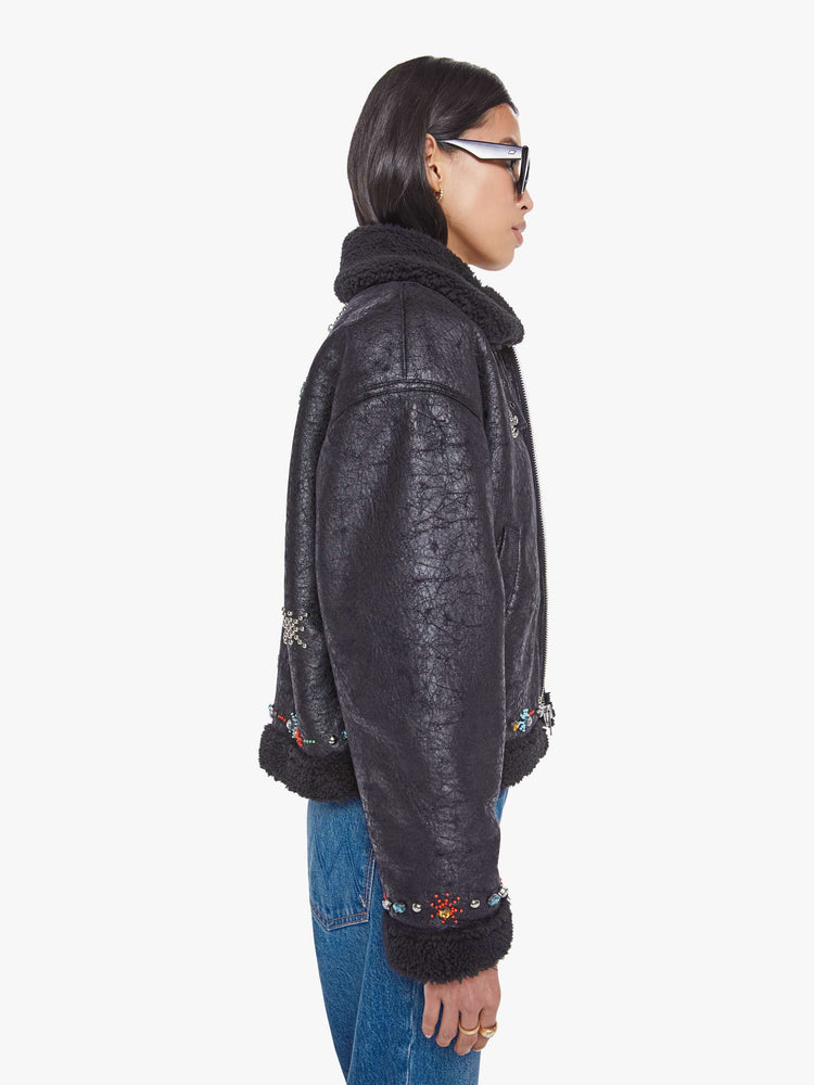 Side view of a woman in metallic black collared zip-up jacket with drop shoulders and a slightly cropped, boxy fit.