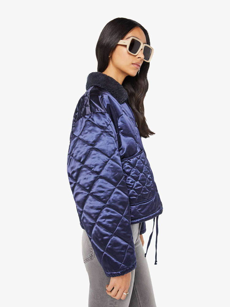 Side view of a woman in quilted collared jacket in an iridescent dark blue with a faux-sherpa collar and tonal buttons.