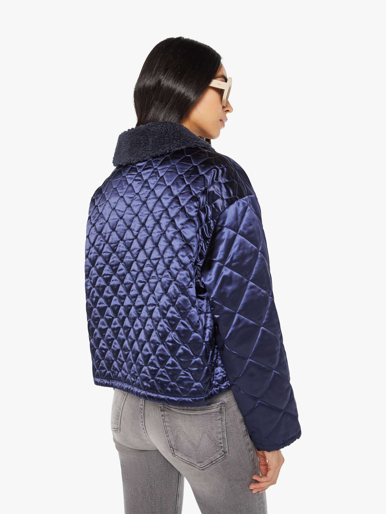 Back view of a woman in quilted collared jacket in an iridescent dark blue with a faux-sherpa collar and tonal buttons.