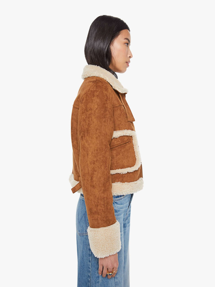 Sid view of a woman in a caramel faux suede  cropped jacket with front patch pockets, buckle details on the collar and sides and a boxy fit. 