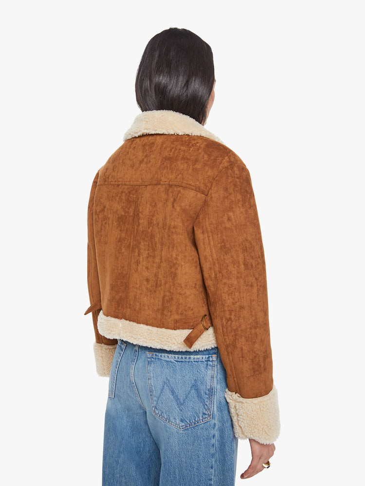 Back view of a woman in a caramel faux suede  cropped jacket with front patch pockets, buckle details on the collar and sides and a boxy fit. 