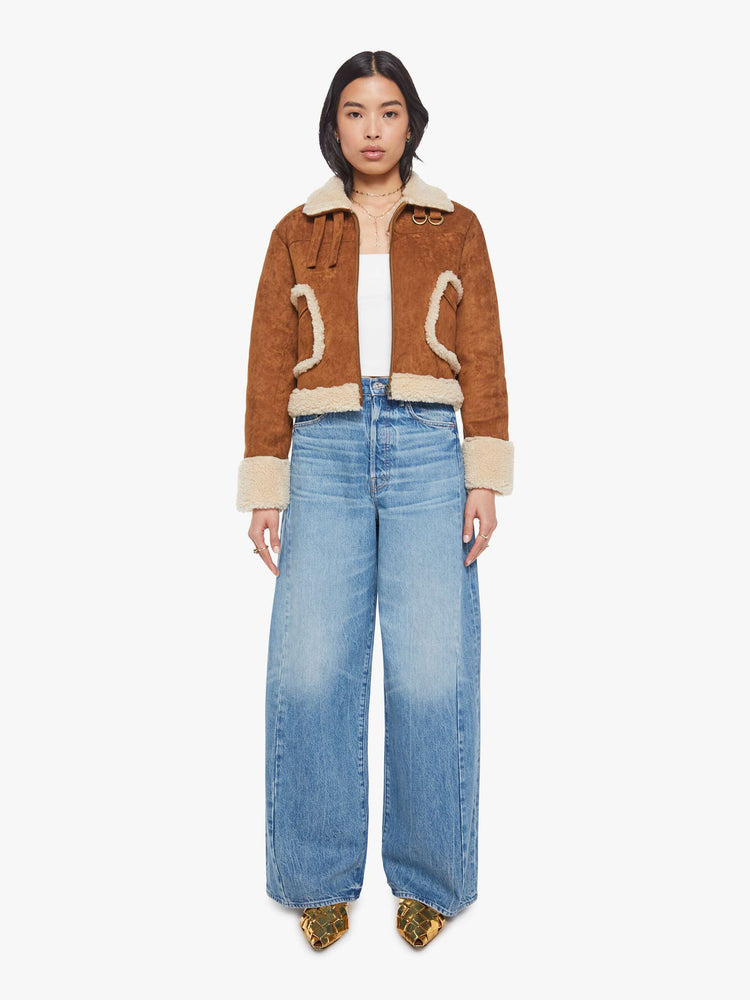 Full body view of a woman in a caramel faux suede  cropped jacket with front patch pockets, buckle details on the collar and sides and a boxy fit. 