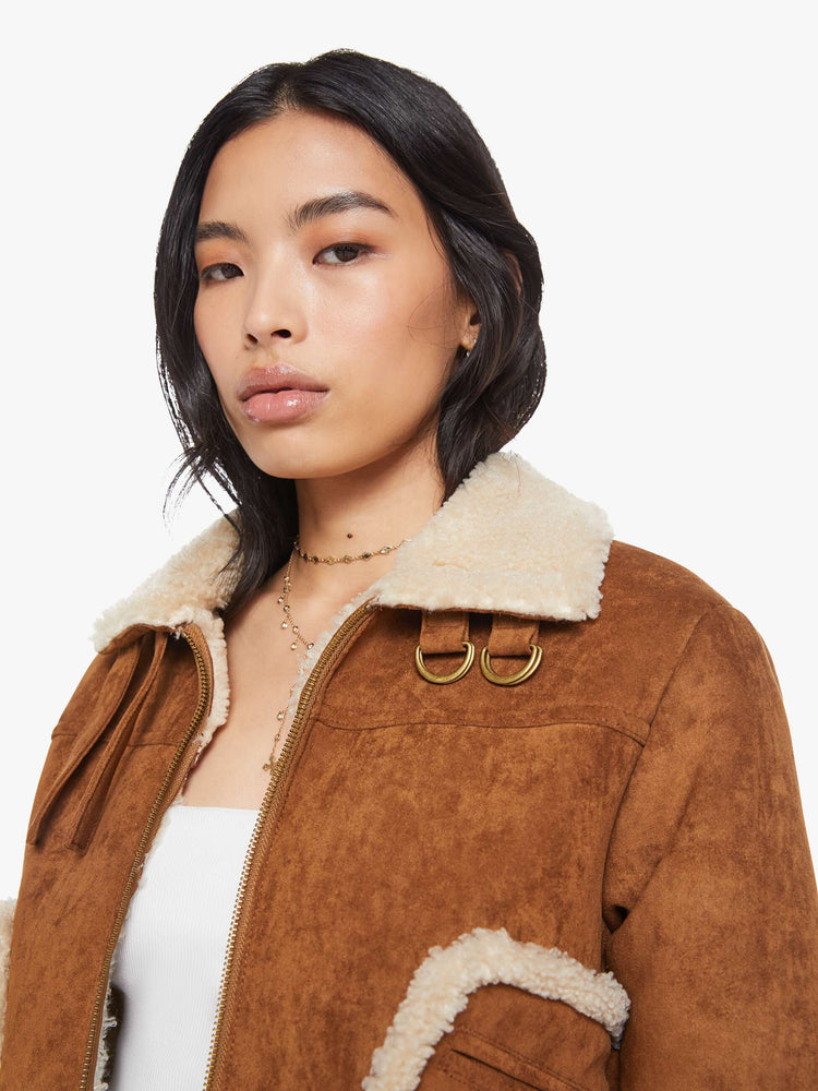 Close up view of a woman in a caramel faux suede  cropped jacket with front patch pockets, buckle details on the collar and sides and a boxy fit. 