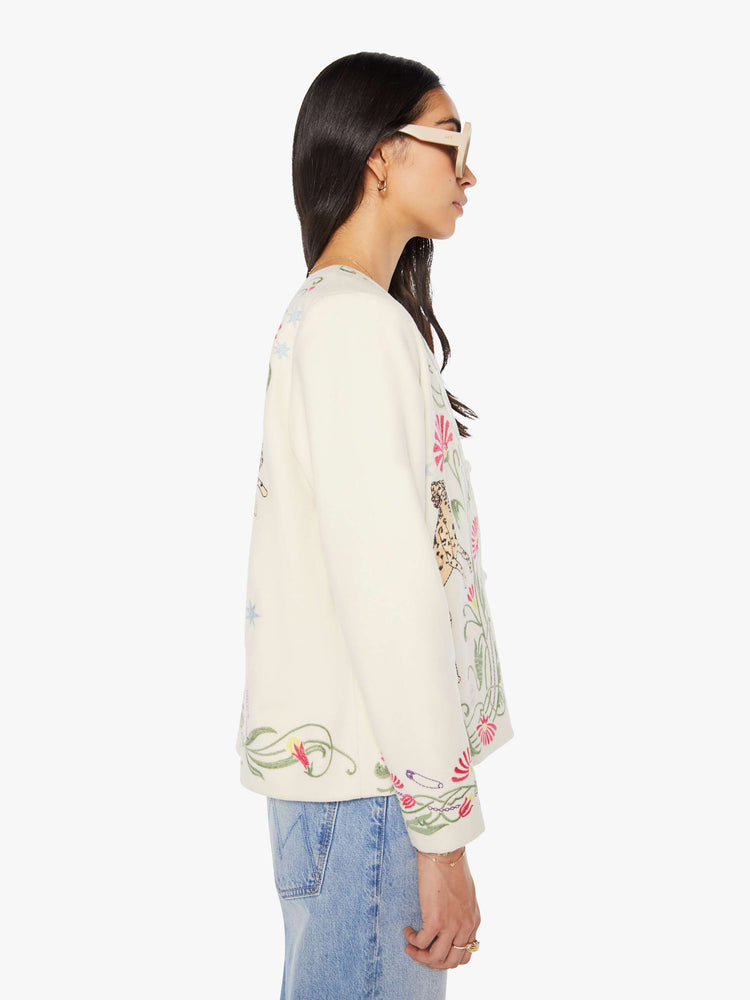Side view of a woman in creamy off-white with floral details cheetahs V-neck jacket with buttons down the front and a loose, boxy fit.