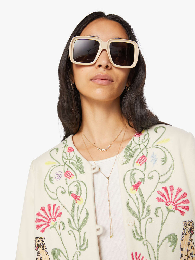 Close up view of a woman in creamy off-white with floral details cheetahs V-neck jacket with buttons down the front and a loose, boxy fit.