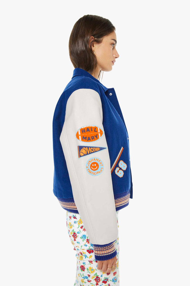 Side view of a woman in navy with off-white sleeves, red striped details and vintage-inspired chenille patches, pins and needlepoint throughout.