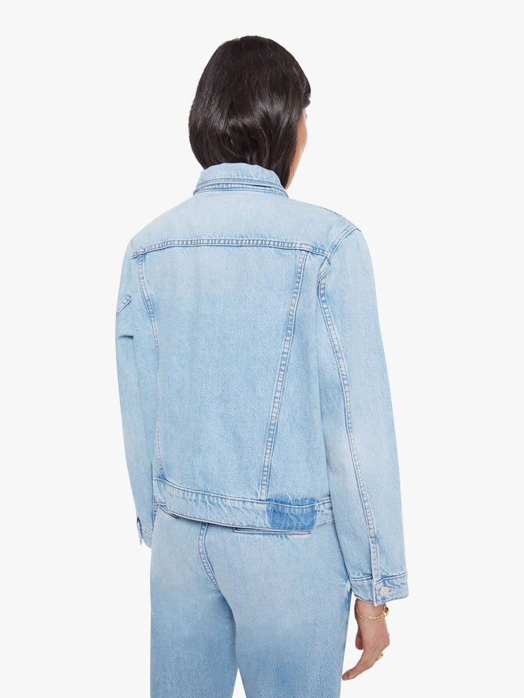Back view of a woman in a light blue denim jacket with front patch pockets and a slightly cropped fit.