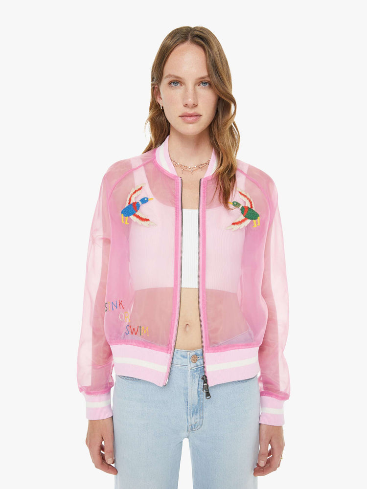 Front view of a woman in a sheer pink jacket with embroidered graphics throughout and "CAMP MOTHER" in red, white and blue text on the back.