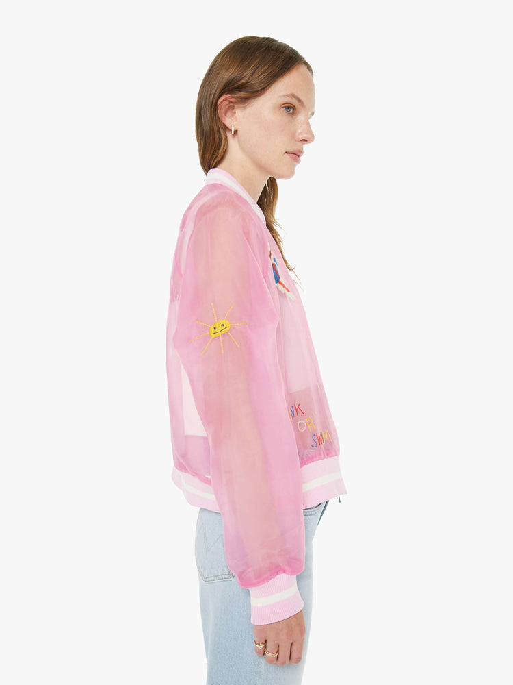 Side view of a woman in a sheer pink jacket with embroidered graphics throughout and "CAMP MOTHER" in red, white and blue text on the back.