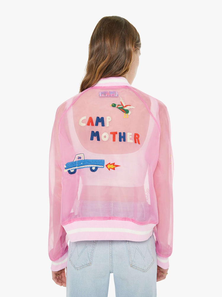 Back view of a woman in a sheer pink jacket with embroidered graphics throughout and "CAMP MOTHER" in red, white and blue text on the back.