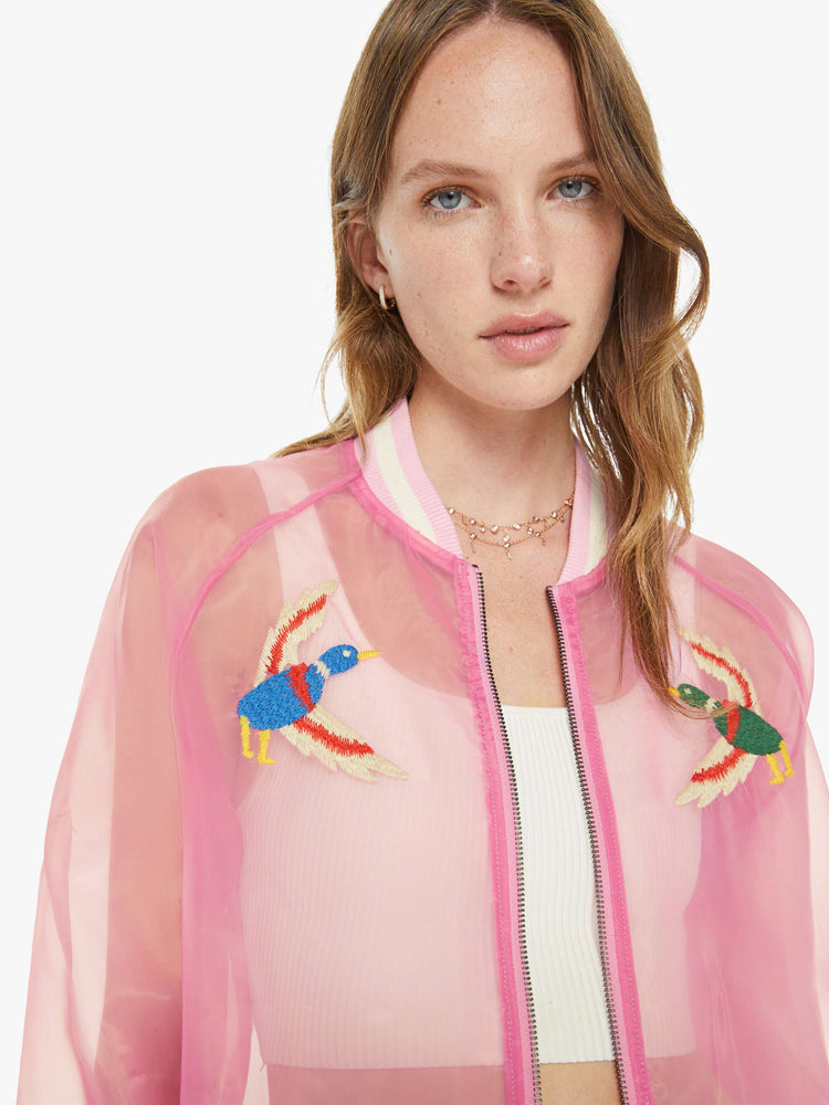 Close up view of a woman in a sheer pink jacket with embroidered graphics throughout and "CAMP MOTHER" in red, white and blue text on the back.