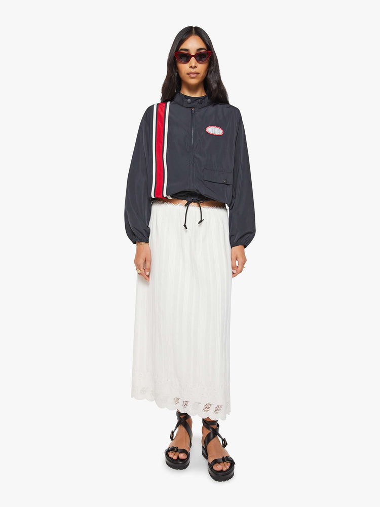 Full body view of a woman in a navy with red and white stripe vintage-inspired windbreaker with a short stacked collar that buttons, a zip closure, drop shoulders, balloon sleeves, a small patch pocket and a cropped drawstring hem.
