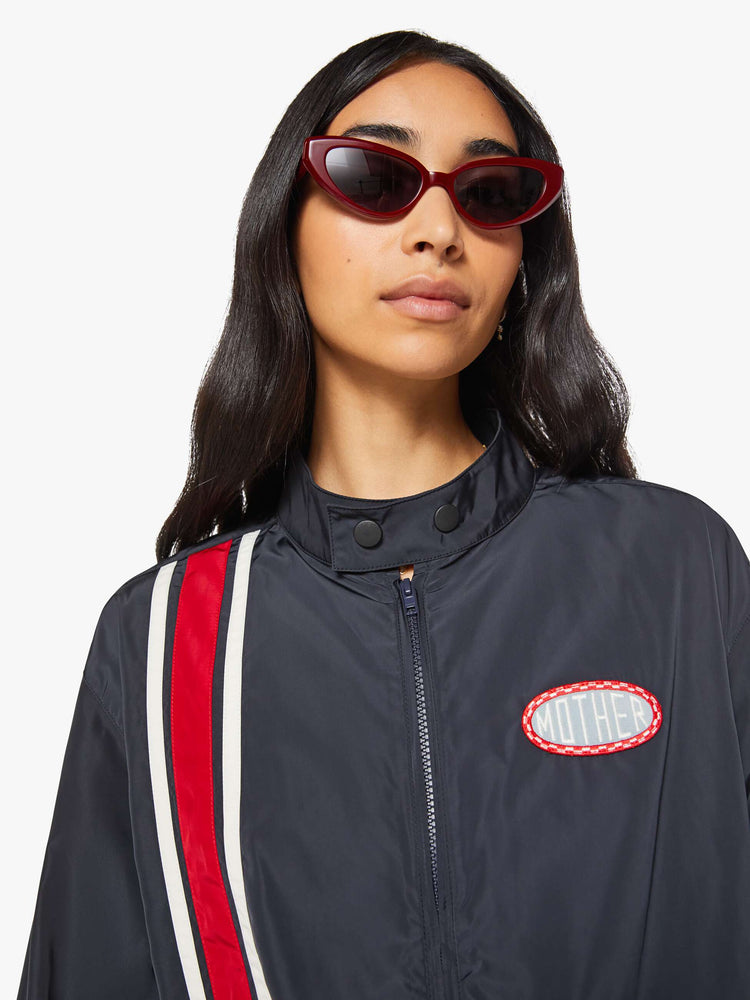 Close up view of a woman in a navy with red and white stripe vintage-inspired windbreaker with a short stacked collar that buttons, a zip closure, drop shoulders, balloon sleeves, a small patch pocket and a cropped drawstring hem.