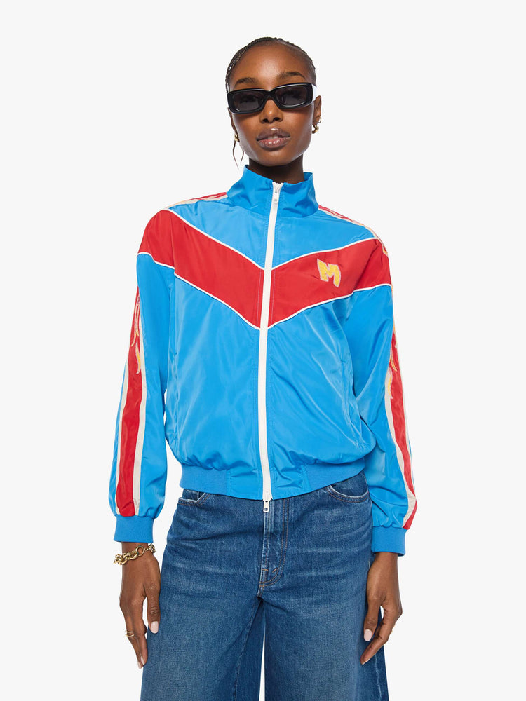Front view of a woman in a glossy vintage blue letterman jacket with angled red panels across the chest, stripes down the sleeves, an M patch in yellow on the front and stitched details along the shoulders.