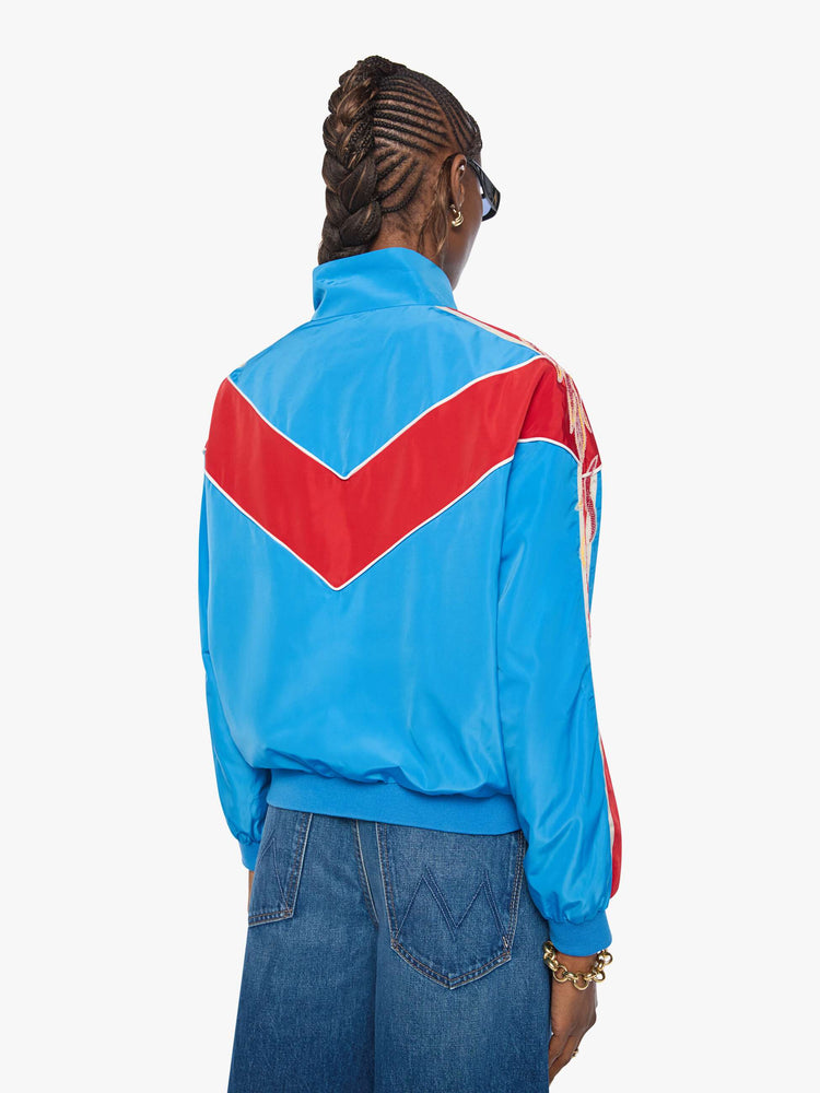 Back view of a woman in a glossy vintage blue letterman jacket with angled red panels across the chest, stripes down the sleeves, an M patch in yellow on the front and stitched details along the shoulders.